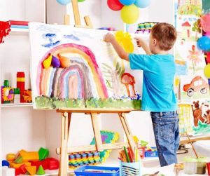 A small boy painting a rainbow in his preschool classroom.
