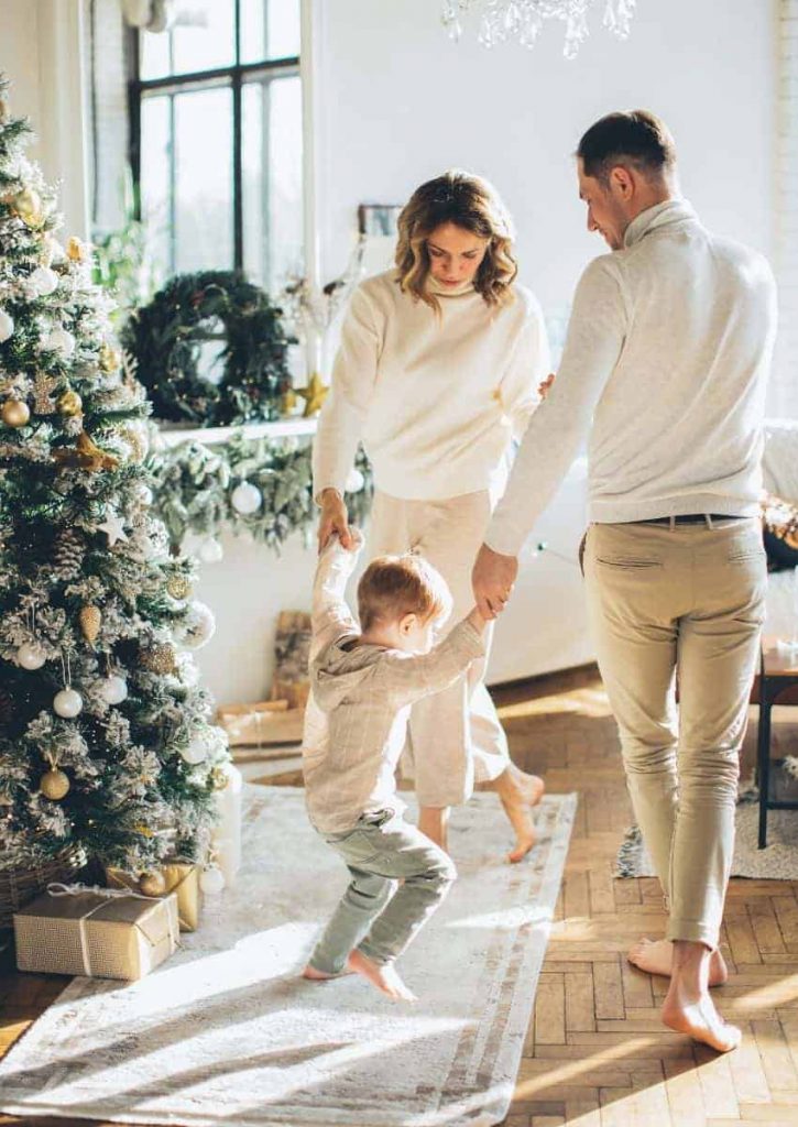 Husband and wife holding son's hand in front of the Christmas tree.