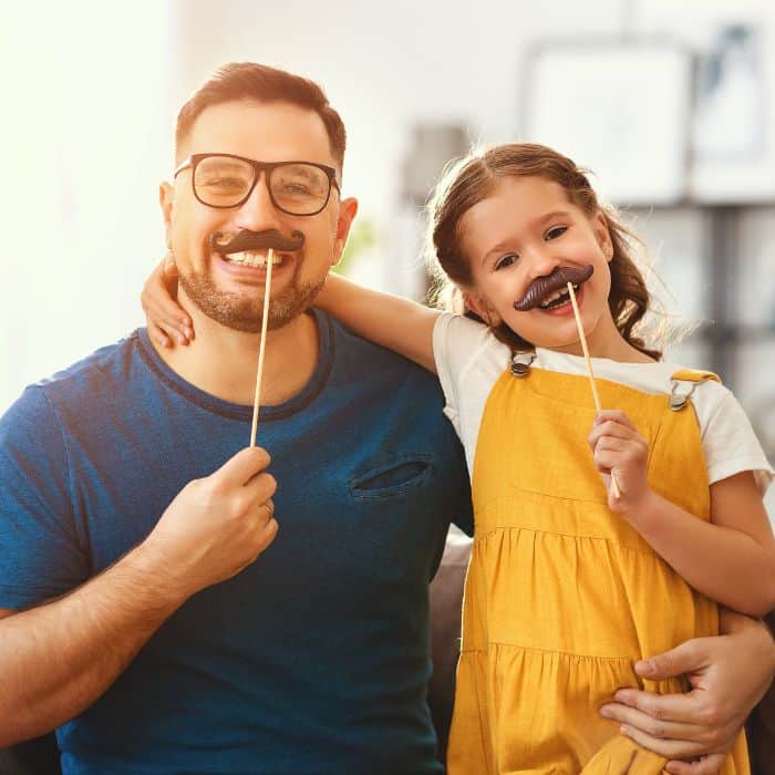 A father and daughter with silly mustache props on their faces.