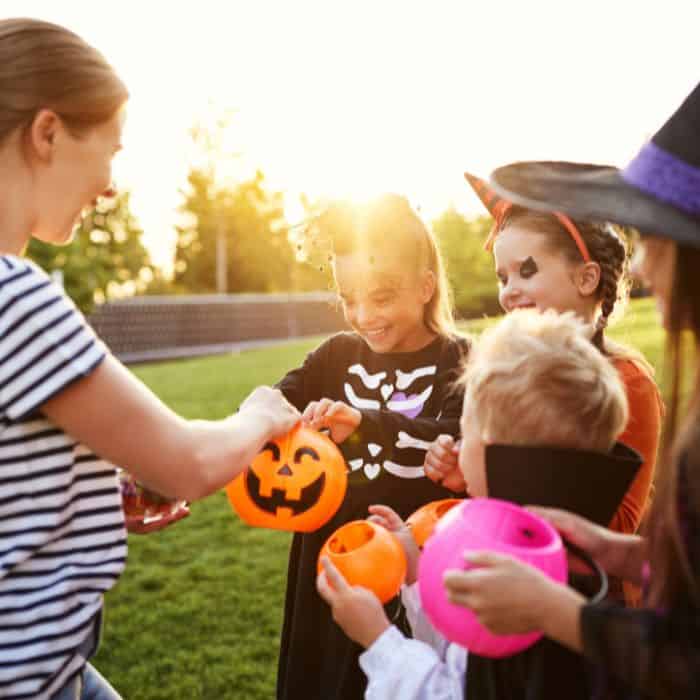 A woman placing treats in children's trick or treat baskets.
