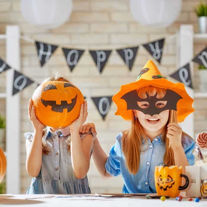 Two children holding up Halloween decorations to their face.