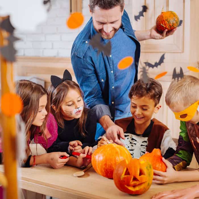 A man helping a group of children with pumpkin carving.