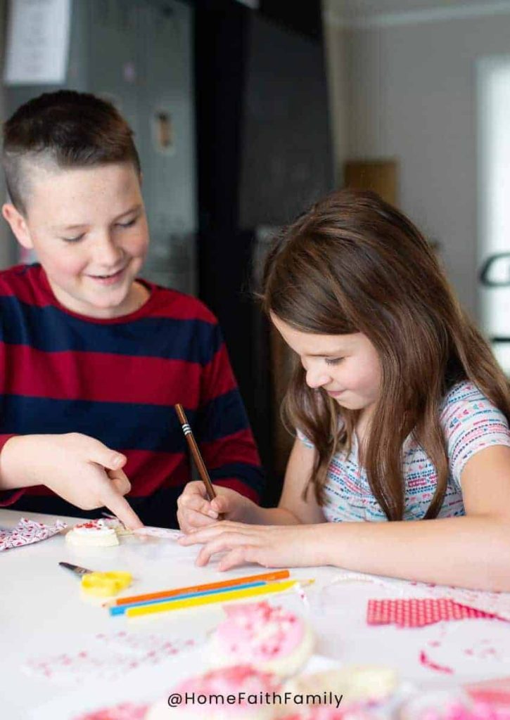 A boy and a girl sitting at a family table working on their I Spy Valentine's Day printables while enjoying a Valentine's Day celebration.