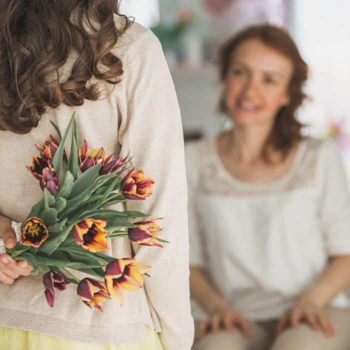 A young woman is holding a bouquet of flowers for her mom.