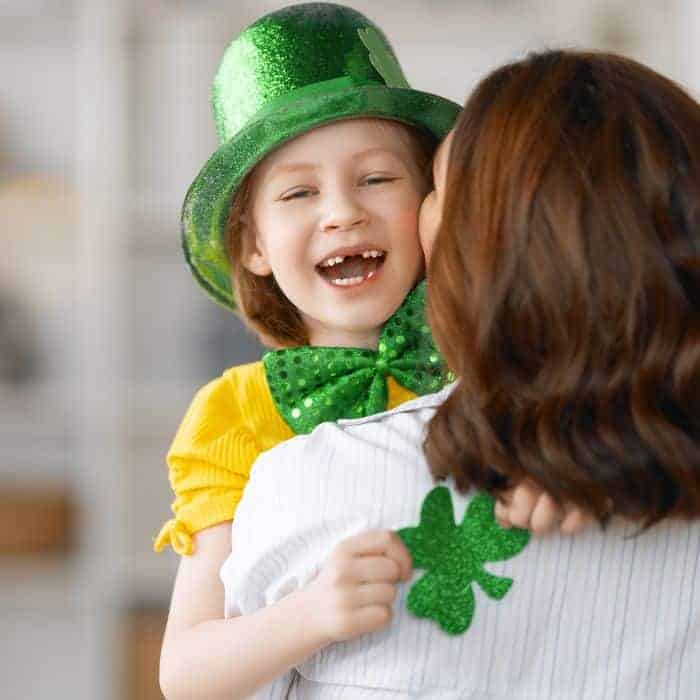 A mother with her preschooler in her arms. The child is wearing a green hat and bow.