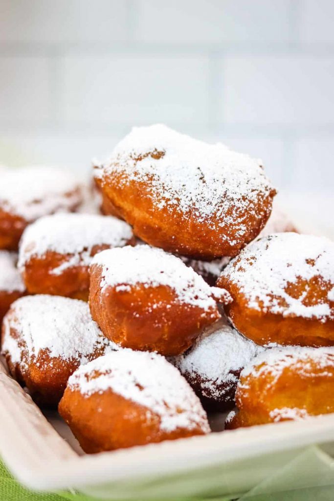A plate of fresh fried beignets with powdered sugar sprinkled on top.