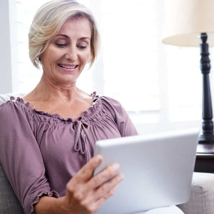A middle aged woman communicating with a family member on her tablet.