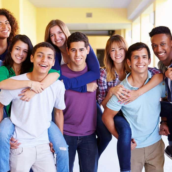 A group of high school students together. Some of the young ladies are on the young men's backs.