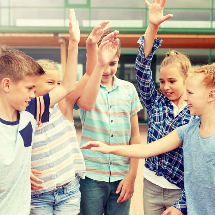 Children high-fiving each other outside their school.