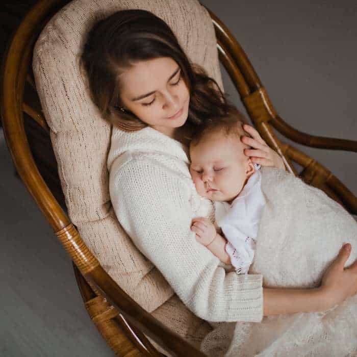 A mother in a rocking chair with her sleeping chubby cheeks baby.