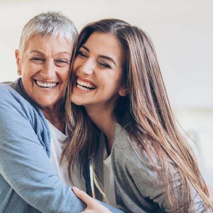 An older woman and her adult daughter embrace for hugs and smile.