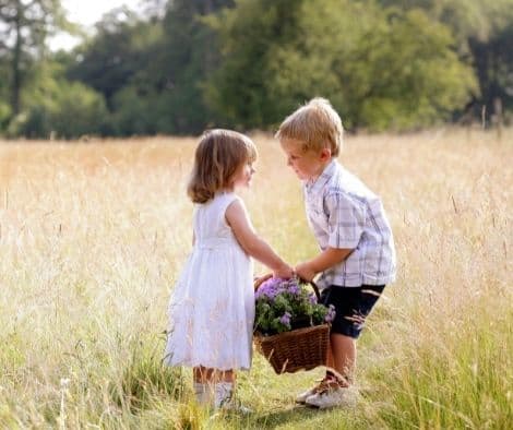 Two children in a field of flowers being kind to teach other.