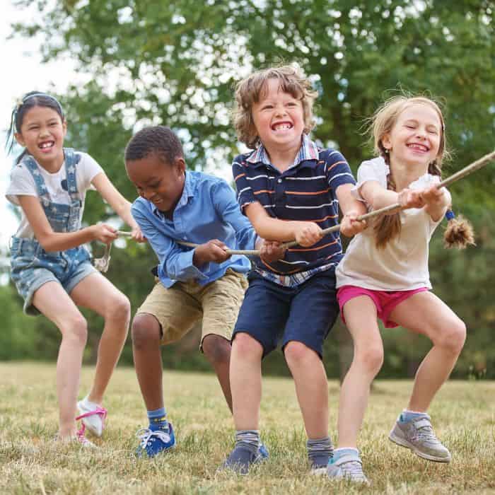 Four children of diverse backgrounds pulling on a rope with joyful expressions in a game of tug-of-war on a grassy field during an LDS activity day.