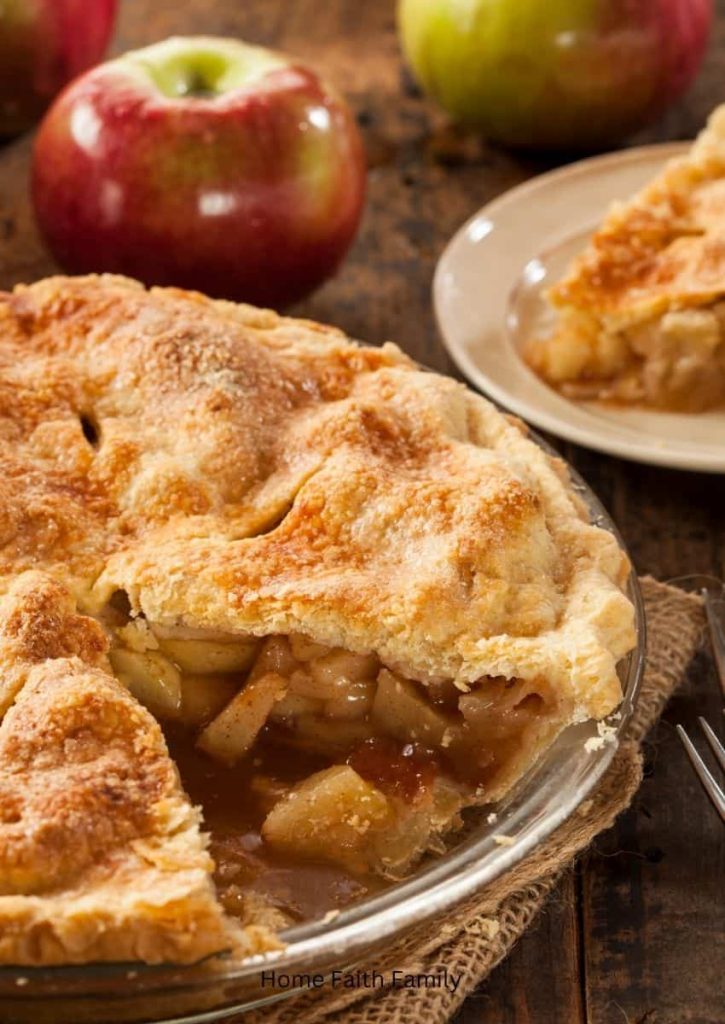 A homemade apple pie with a slice cut out of the main pie dish.