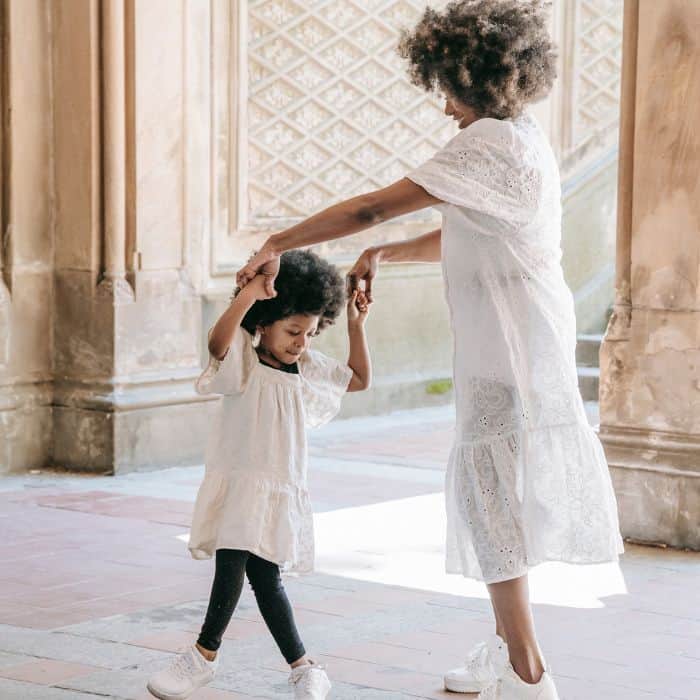 A joyful moment between mother and daughter, dancing hand-in-hand under the warm glow of sunlight filtering through an elegant archway.