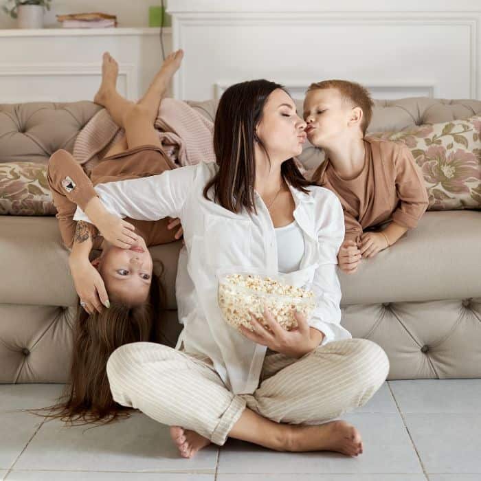 A mom with a bowl of popcorn spending time with her son and daughter.