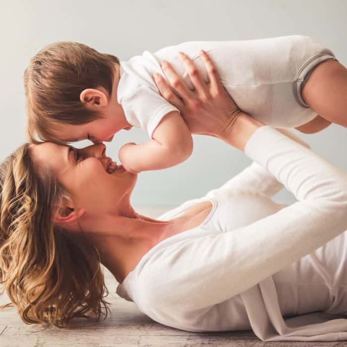 A young mother holding up her baby son above her head and stomach.