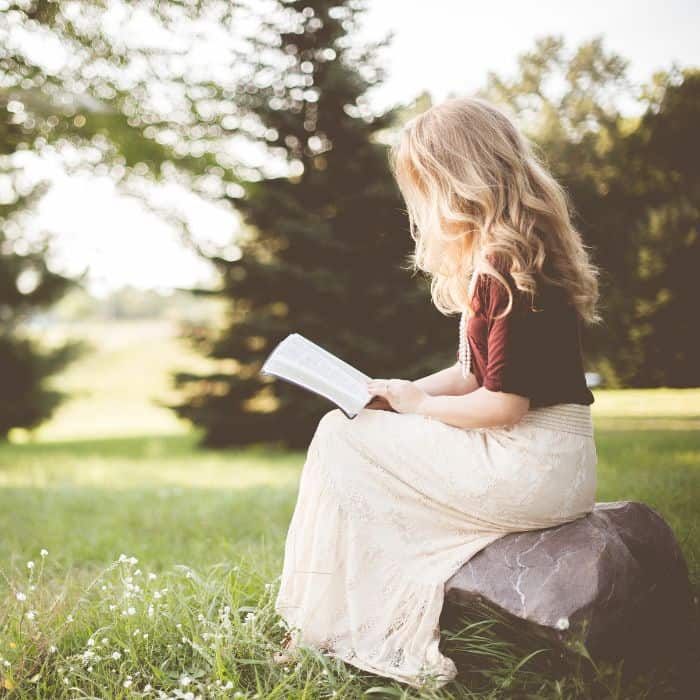 A young woman sitting on a rock while reading her Bible.