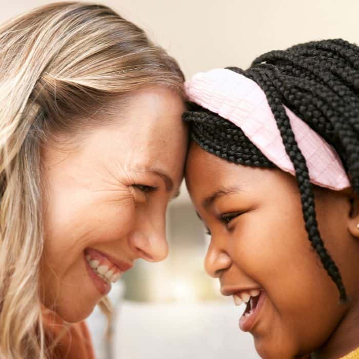 A mom is touching foreheads with her daughter. Both are smiling.