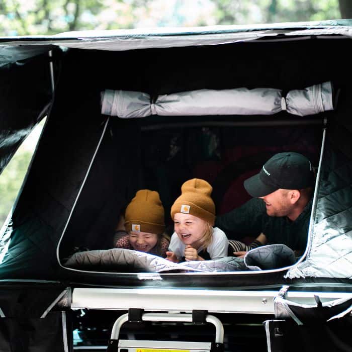 A father with his two daughters camping in their car.