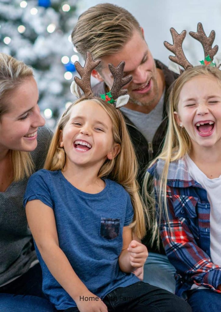 A family laughing together. The little girls are wearing reindeer headbands on their head.