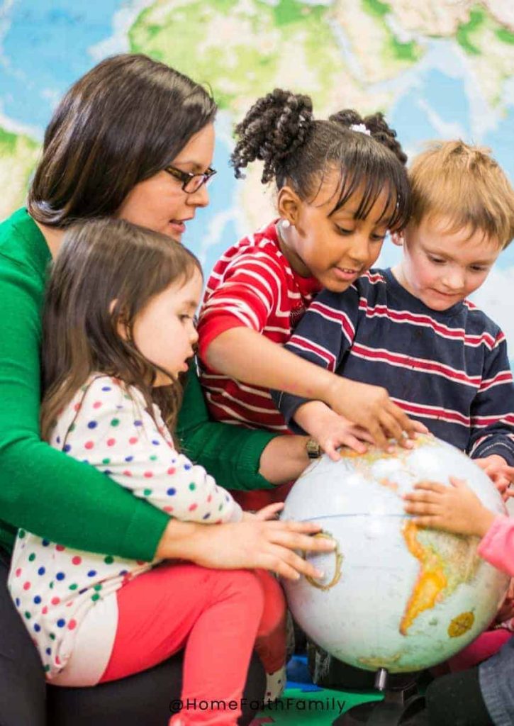 A childcare worker surrounded by children pointing to a globe during a lesson.