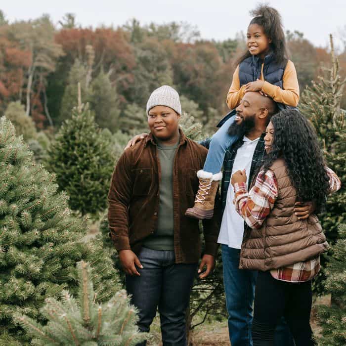 A husband and wife with their son and daughter. The family is walking through a Christmas tree farm.