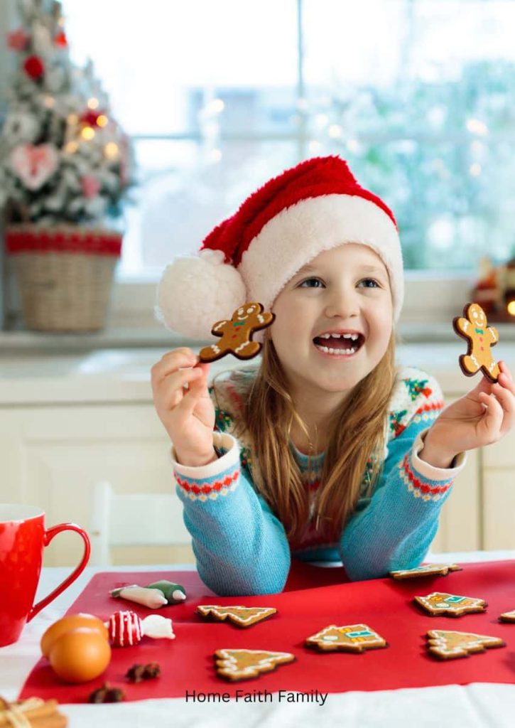 A little girl holding up a few gingerbread men at the kitchen table.