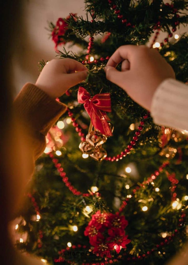 A child's hand placing a Christmas ornament on the tree.