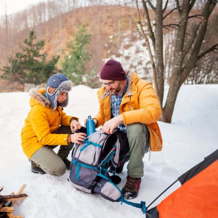 A dad and son camping in the snow and cold weather.