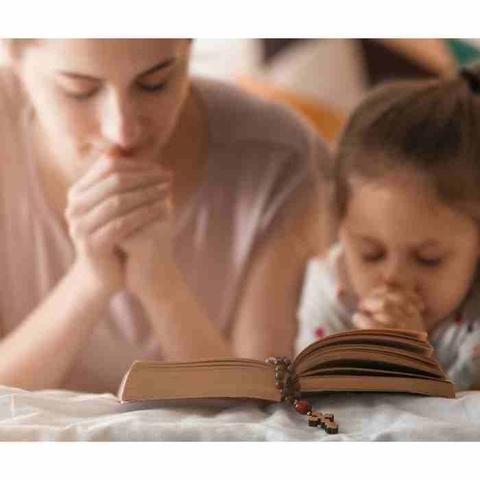 A mother praying with her young daughter over the Bible.