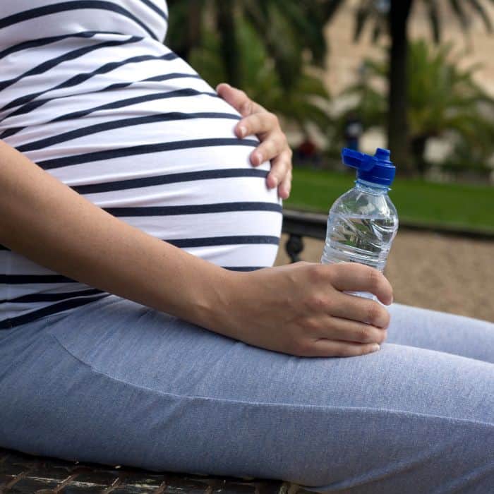 Pregnant woman sitting down with a water bottle.