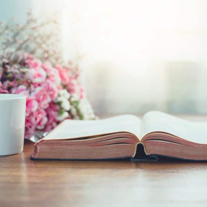 An open Bible on the table with a bouquet of flowers and a cup of coffee.