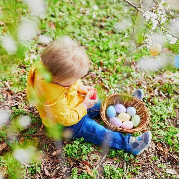 A 1 year old sitting in the grass with an Easter basket filled with Easter eggs.