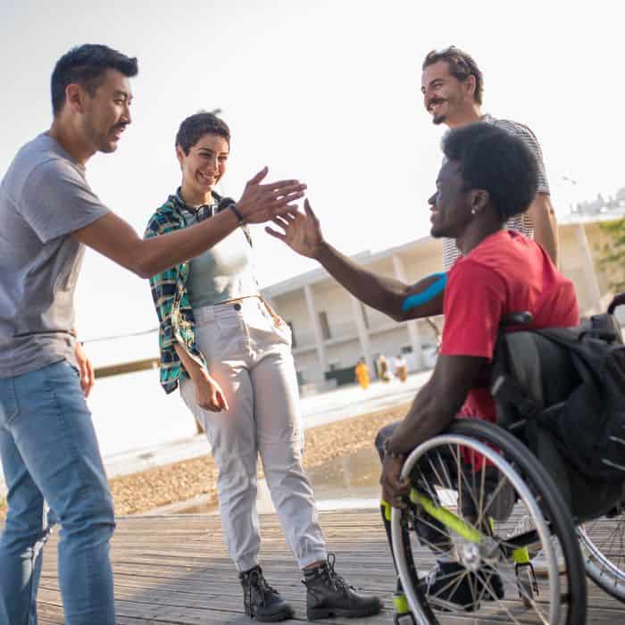 A group of friends at the basketball court. One main, in a wheelchair, is giving a high five to another man.