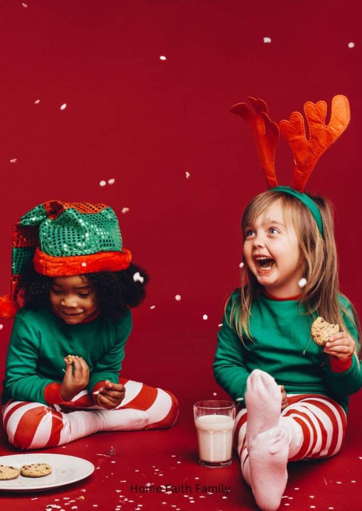 Two little girls eating Christmas cookies and dressed as elves. Both are smiling and laughing together.