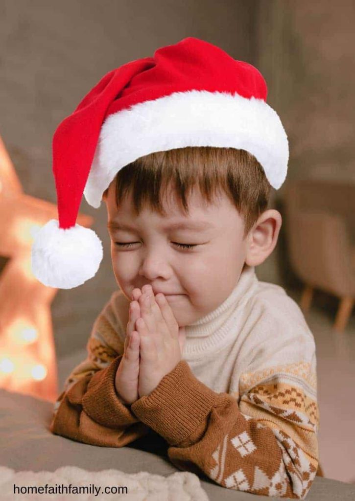 Little boy wearing a santa hat and praying by his bedside.