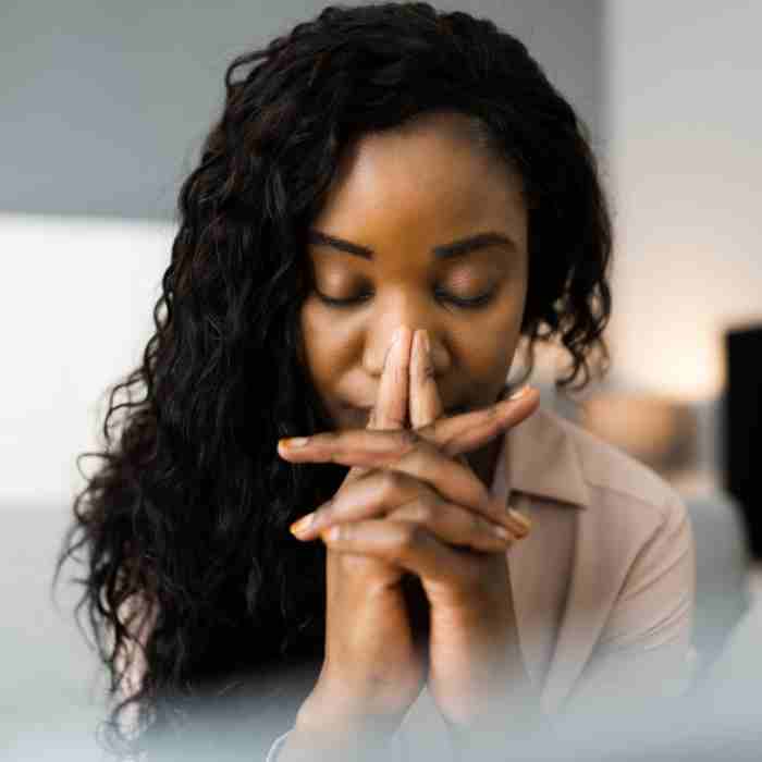 A woman with her hands folded up to her face while she prays.