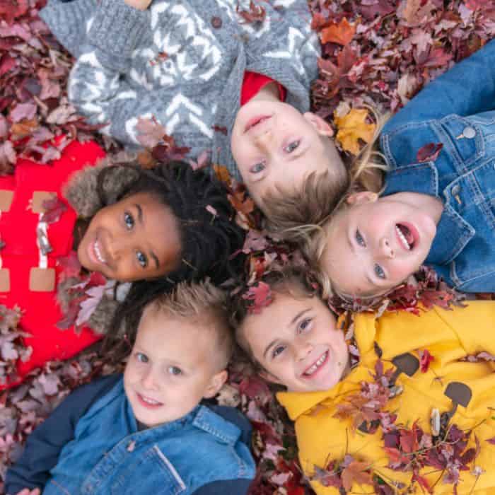 A group of young kids laying down in the fall leaves.