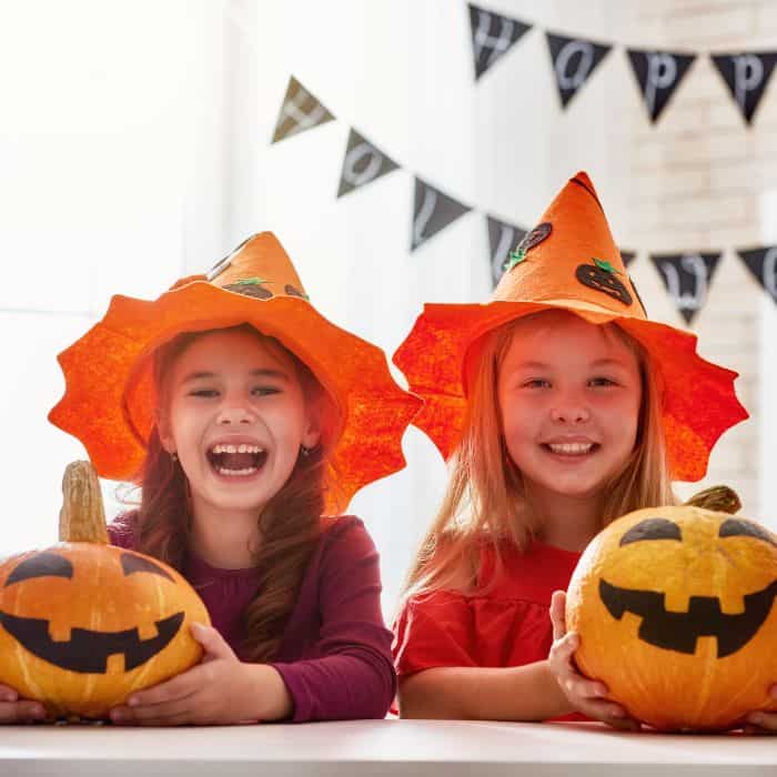 Two little girls with orange witch hats and pumpkins.