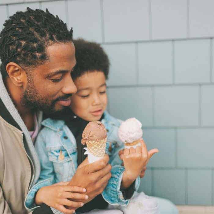A young dad eating ice cream with his son.
