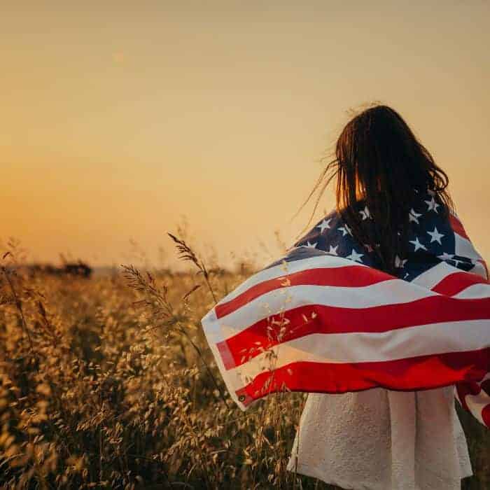 A woman draped in an American flag standing in a wheat field.