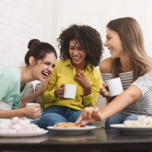 A group of women laughing and drinking coffee together.