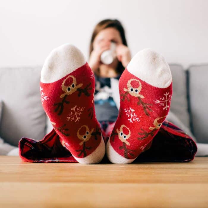 A woman sitting on her couch while wearing fuzzy Christmas socks.