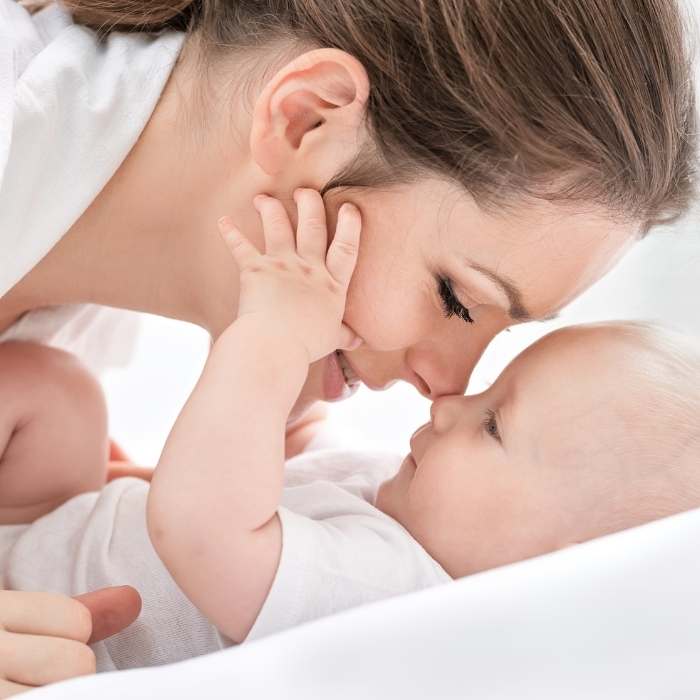 A woman nose to nose with her newborn baby who is placing their hands on the mother's face.