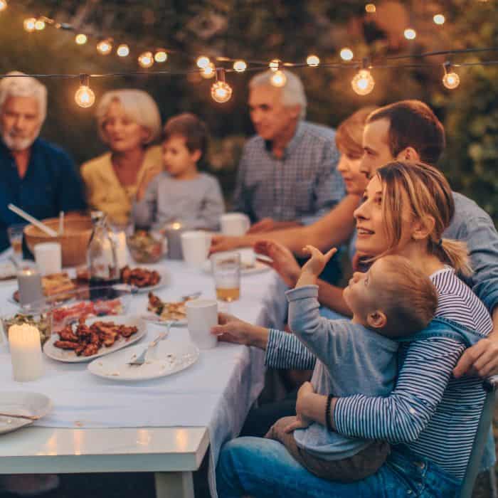 A little boy sitting on his mothers lap. They are eating dinner with the entire extended family outside.