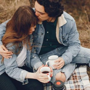 A young couple snuggling on a fall blanket with cups of coffee.