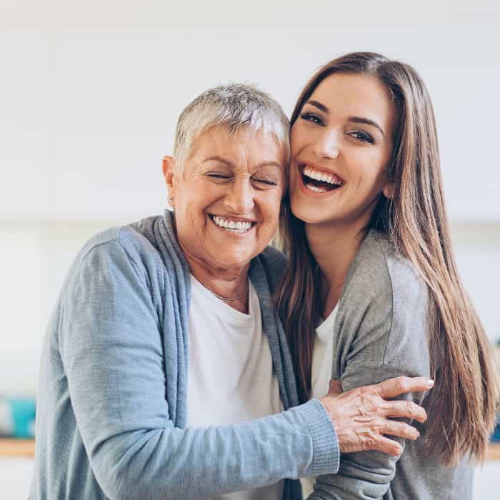 An older and a younger woman embracing and smiling with each other.