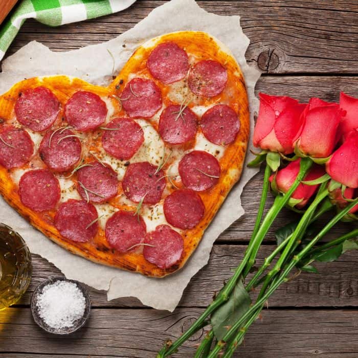 A heart shaped pizza laying next to a dozen roses.