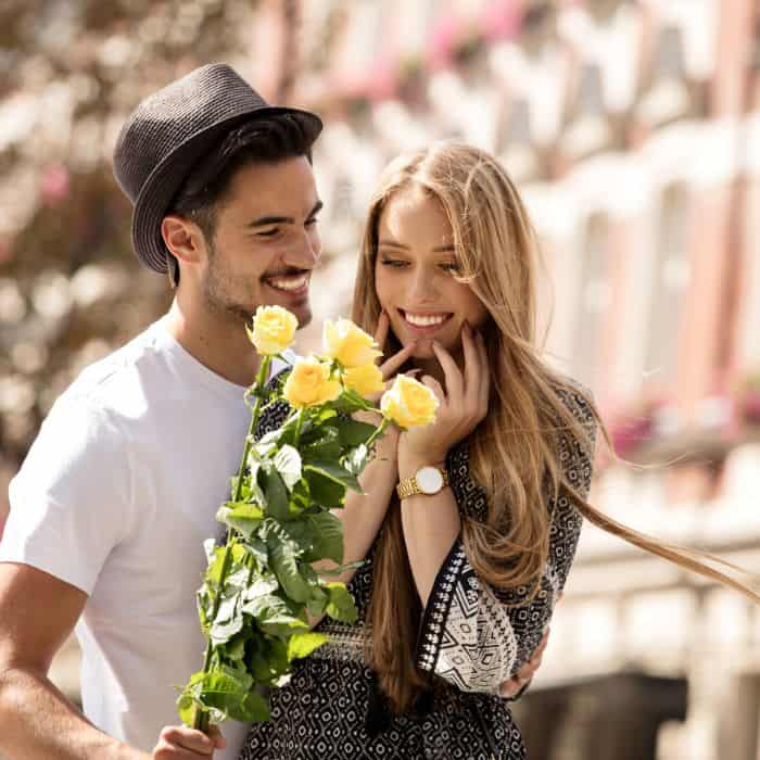 A man handing a bouquet of yellow flowers to a smiling woman.